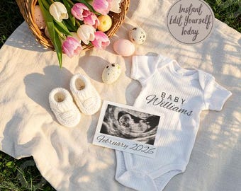 Könnte beinhalten: Ein weißer Strampler mit dem Text "BABY Williams" darauf, ein weißes Ultraschallbild mit dem Datum "Februar 2026" und zwei weiße gestrickte Babyschuhe auf einer weißen Decke mit rosa und weißen Blumen.