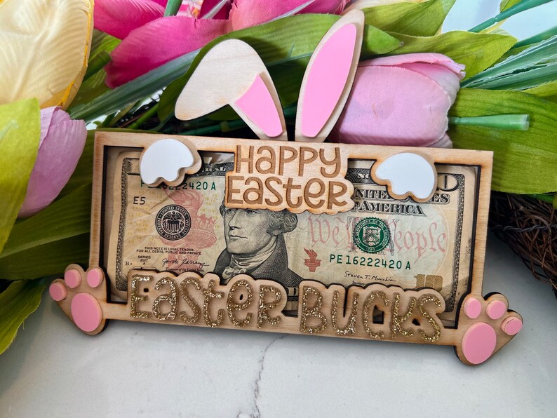 May include: A wooden Easter money holder with a bunny ear design. The holder has a slot for a dollar bill and says "Happy Easter" and "Easter Bucks".