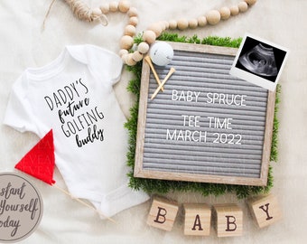 Puede incluir: Un body blanco con el texto "Daddy's future golfing buddy" en él. Un tablero de letras con el texto "Baby Spruce Tee Time March 2022" y una pequeña imagen de ultrasonido. Un conjunto de bloques de madera que deletrean "BABY".