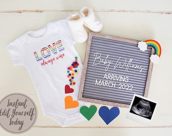 Può includere: Un body bianco con le parole "LOVE always wins" in lettere arcobaleno. Una lavagna con il testo "Baby Williams Arriving March 2022" e un arcobaleno con le nuvole sono su una superficie bianca.