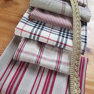 May include: A stack of six fabric swatches in various plaid and striped patterns featuring red, white, and gray colors. A gold trim is visible on the right side of the image.