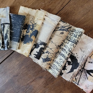 Puede incluir: Una colección de recortes de tela con diseños impresos en blanco y negro, incluyendo texto e imágenes de pájaros y ramas. La tela es de color beige claro con una superficie ligeramente texturizada.