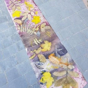 Peut inclure: Un long tissu rectangulaire avec un fond rose et un motif de feuilles press&eacute;es dans des tons de jaune, brun et vert.