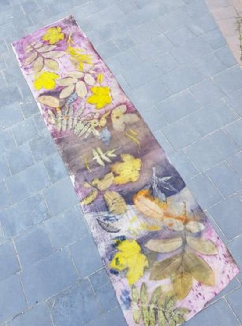 Peut inclure: Un long tissu rectangulaire avec un fond rose et un motif de feuilles press&eacute;es dans des tons de jaune, brun et vert.