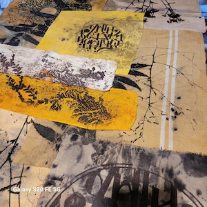 Peut inclure: Œuvre textile abstraite composée de divers morceaux de tissu jaunes, beiges et gris. Les tissus présentent des motifs imprimés, notamment des éléments botaniques et des motifs circulaires avec du texte. L'ensemble est artistique et texturé.
