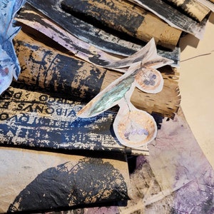 Może przedstawiać: Stos brązowego papieru z czarnym atramentem i tekstem, ułożony warstwami z kawałkiem papieru z zielonym i złotym wzorem liścia i dwoma złotymi k&oacute;łkami.