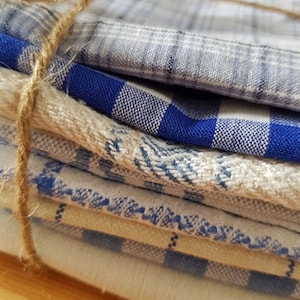 Può includere: Un mucchio di asciugamani da cucina a quadri blu e bianchi legati insieme con uno spago. Gli asciugamani sono realizzati in un tessuto morbido e assorbente e sono perfetti per asciugare piatti, mani e superfici.