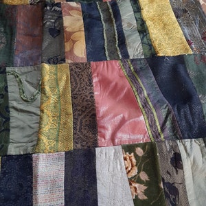 Könnte beinhalten: Ein Patchwork-Deckenbezug aus verschiedenen Stoffen in Grün-, Braun-, Gold- und Rosatönen. Die Decke besteht aus rechteckigen Stoffstücken, die zusammengenäht wurden, um ein einzigartiges und strukturiertes Design zu schaffen.