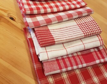 Pode incluir: Um conjunto de seis toalhas de cozinha xadrez vermelhas e brancas. As toalhas estão dobradas e empilhadas sobre uma superfície de madeira.