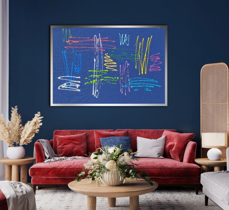 K&ouml;nnte beinhalten: Ein gerahmter abstrakter Kunstdruck mit bunten Linien und Formen auf blauem Hintergrund. Der Druck h&auml;ngt an einer dunkelblauen Wand &uuml;ber einem roten Samtsofa.