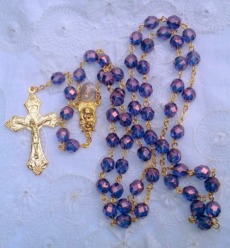 May include: A gold rosary with purple glass beads. The rosary features a gold crucifix with a figure of Jesus Christ.