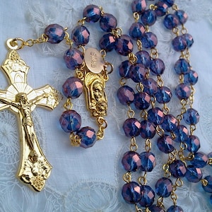 May include: A gold rosary with blue glass beads. The crucifix features a gold figure of Jesus Christ.