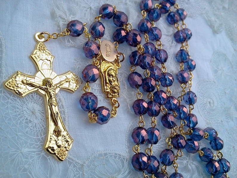 May include: A gold rosary with blue glass beads. The crucifix features a gold figure of Jesus Christ.