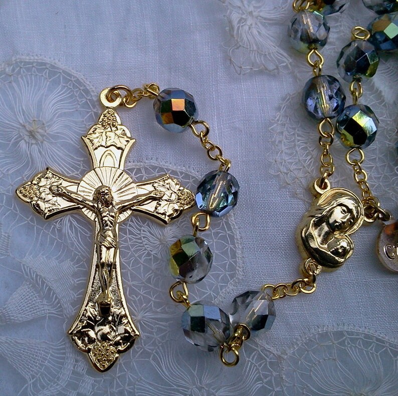 May include: A gold rosary with a detailed crucifix and a silver-toned pendant featuring the Virgin Mary and baby Jesus. The beads are iridescent and have a blue-green hue.