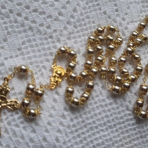 以下が含まれることがあります： 金色のロザリオに銀色のビーズがついたもの。ロザリオには金色の十字架と金色のセンターピースがついています。