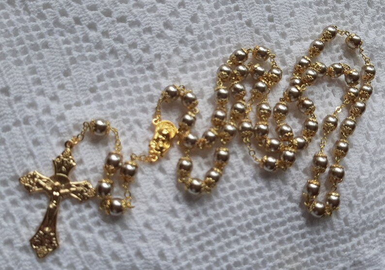 以下が含まれることがあります： 金色のロザリオに銀色のビーズがついたもの。ロザリオには金色の十字架と金色のセンターピースがついています。