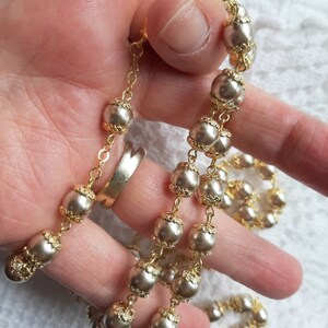 以下が含まれることがあります： 白い真珠のようなビーズが付いた金のチェーンネックレス。ビーズはテクスチャ加工された金の縁取りが施されています。