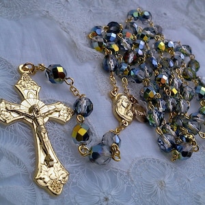 May include: A gold-toned rosary with a crucifix and a small medal. The beads are made of iridescent blue glass.