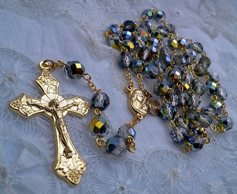 May include: A gold-toned rosary with a crucifix and a small medal. The beads are made of iridescent blue glass.