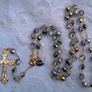 May include: A gold chain rosary with a silver crucifix and blue crystal beads. The beads are faceted and have a rainbow iridescent sheen. The tag on the chain reads "Czech".