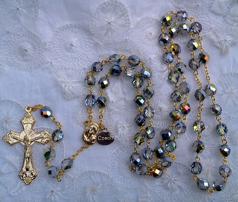 May include: A gold chain rosary with a silver crucifix and blue crystal beads. The beads are faceted and have a rainbow iridescent sheen. The tag on the chain reads "Czech".