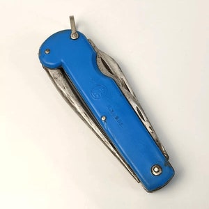 Op de afbeelding: Een blauw en zilver multi-tool mes met een opvouwbaar ontwerp. Het mes heeft een helderblauwe handgreep en verschillende zilverkleurige gereedschappen. De tekst "1.2.50K." staat op de handgreep. Aan het uiteinde van de handgreep zit een kleine metalen lus.