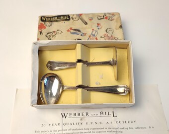 May include: A set of three silver baby spoons in a white box with a colorful design. The box has the text "Webber and Hill 20 Year Quality E.P.N.S. A.I Cutlery" printed on it.