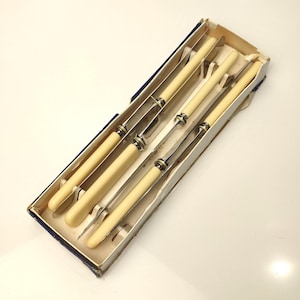 May include: A set of six vintage knives in a rectangular box. The knives have ivory-colored handles and silver blades. The box is made of cardboard with a blue and white trim.