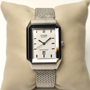 Könnte beinhalten: Eine silberne Citizen Quartz-Uhr mit rechteckigem Zifferblatt und Mesh-Armband. Das weiße Zifferblatt hat schwarze Zeiger, rechteckige Stundenmarkierungen und den Text "CITIZEN QUARTZ" und "WATER RESIST". Das Datum wird als "25" angezeigt.