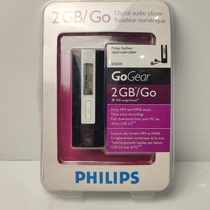 Pu&ograve; includere: Un lettore audio digitale Philips GoGear nella sua confezione originale. Il lettore &egrave; bianco e nero, con un piccolo schermo e pulsanti. La confezione &egrave; in plastica trasparente con un inserto rosa e bianco e include il testo "2 GB/Go".