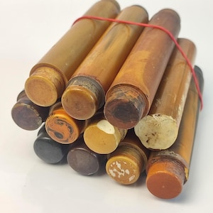 Puede incluir: Un conjunto de tapones de botella de madera vintage, en tonos marrones y beige, sujetos con una goma elástica roja. Los tapones tienen forma cilíndrica con tapas de varios colores.