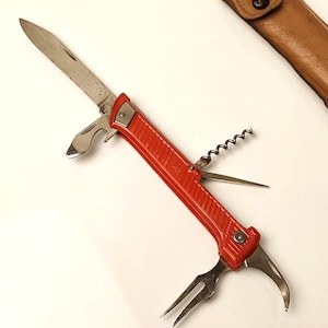 以下が含まれることがあります： 刃、栓抜き、コルク抜き、フォーク、小型のこぎり付きの赤いマルチツールポケットナイフ。ナイフは閉じており、革製の鞘が付いています。