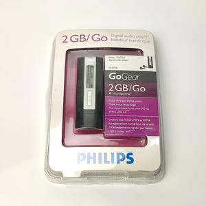 Pu&ograve; includere: Un lettore audio digitale Philips GoGear 2GB/Go nella sua confezione originale. Il lettore &egrave; nero e argento, con il testo "GoGear" e "2GB/Go" visibili. La confezione include testo in inglese e francese.