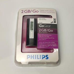 Pu&ograve; includere: Un lettore audio digitale Philips GoGear nella sua confezione originale. Il lettore &egrave; nero e argento, con un piccolo schermo. La confezione indica una capacit&agrave; di 2 GB e presenta il logo Philips.
