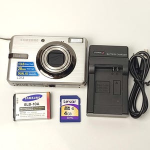 Peut inclure: Appareil photo numérique Samsung L313 argenté avec une résolution de 13,6 mégapixels, un objectif grand angle de 28 mm et une double stabilisation d'image. Comprend une batterie, une carte mémoire SDHC de 4 Go et un chargeur.