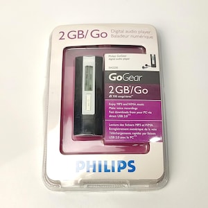 May include: A Philips GoGear digital audio player in its original packaging. The package is white and purple, with the text "2 GB/Go" and "Digital audio player" visible. The player itself is black and silver.