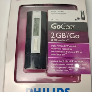 Pu&ograve; includere: Un lettore audio digitale Philips GoGear nella sua confezione originale. Il lettore nero ha un piccolo schermo che mostra le informazioni sulla canzone. La confezione include il testo "2 GB/Go" e "930 canzoni/titoli".