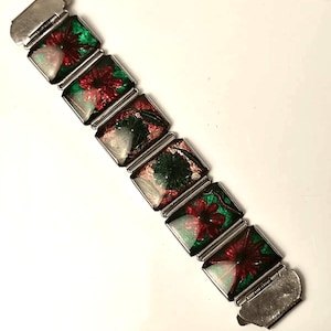 May include: A silver bracelet with a hinged clasp. The bracelet is decorated with six square-shaped, colorful enamel tiles featuring floral designs in shades of red, green, and white.