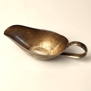 May include: A silver gravy boat with a handle. The boat is oval shaped and has a smooth, shiny surface.