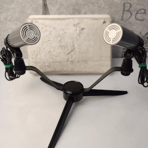 May include: A black microphone stand with two silver microphones attached. The stand has three legs and a round base.