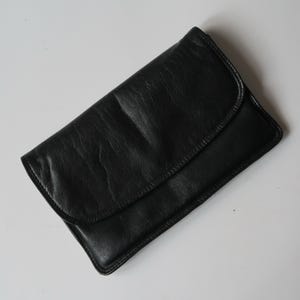 Puede incluir: Un bolso de mano de cuero negro con cierre de solapa.