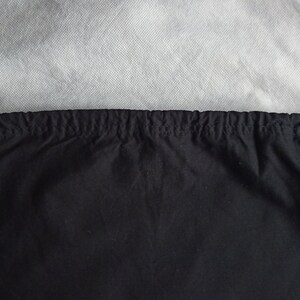 May include: A black drawstring bag with a gathered top and black cord ties. The bag is made of a dark fabric and is set against a light gray background. The drawstring cords are looped at the top.