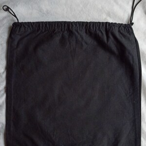May include: A black drawstring bag made of fabric. The bag has a rectangular shape with a gathered top and black drawstrings. The background is a light gray fabric.