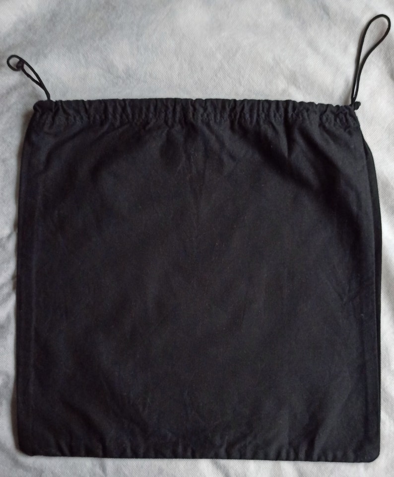 May include: A black drawstring bag made of fabric. The bag has a rectangular shape with a gathered top and black drawstrings. The background is a light gray fabric.