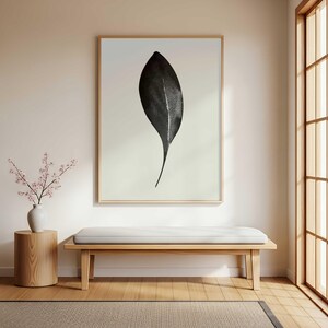 Könnte beinhalten: Ein großer gerahmter Druck mit einem schwarzen Blatt mit weißer Ader. Das Kunstwerk hängt über einer Holzbank mit weißem Kissen. Eine Vase mit rosa Blumen steht auf einem hölzernen Beistelltisch. Der Raum hat eine neutrale Farbpalette.