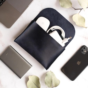 Könnte beinhalten: Ein marineblauer Tech-Organizer aus Leder mit gewölbter Oberseite, der eine weiße Maus, ein Ladegerät und Kabel enthält. Ein schwarzes Smartphone, ein grauer Laptop und eine graue Powerbank sind ebenfalls sichtbar. Die Artikel sind auf einer Marmoroberfläche angeordnet.