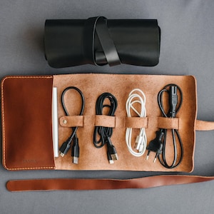 May include: A brown leather cord organizer with a strap closure. The organizer has five slots for cords and a label that says "AIMS".
