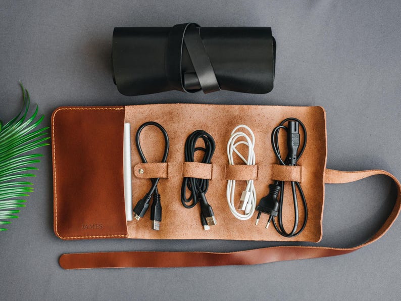 May include: A brown leather cord organizer with a strap closure. The organizer has five slots for cords and a label that says "AIMS".