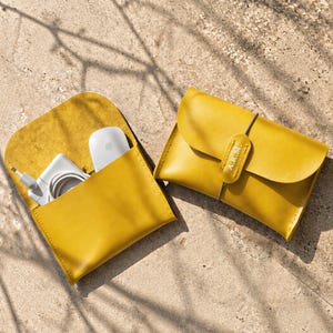 May include: Two mustard yellow leather pouches with rounded flaps. One pouch is open, revealing a white power adapter and a white computer mouse inside. The other pouch is closed with a thin elastic band and features a leather tab with the text A.R.M.