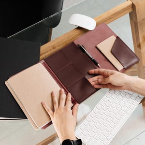 Peut inclure: Une couverture d'agenda en cuir bordeaux foncé dotée de multiples poches intérieures, d'un passant pour stylo avec un stylo noir et d'un carnet beige. L'organiseur comprend une fente dédiée pour les cartes et une fermeture à rabat.